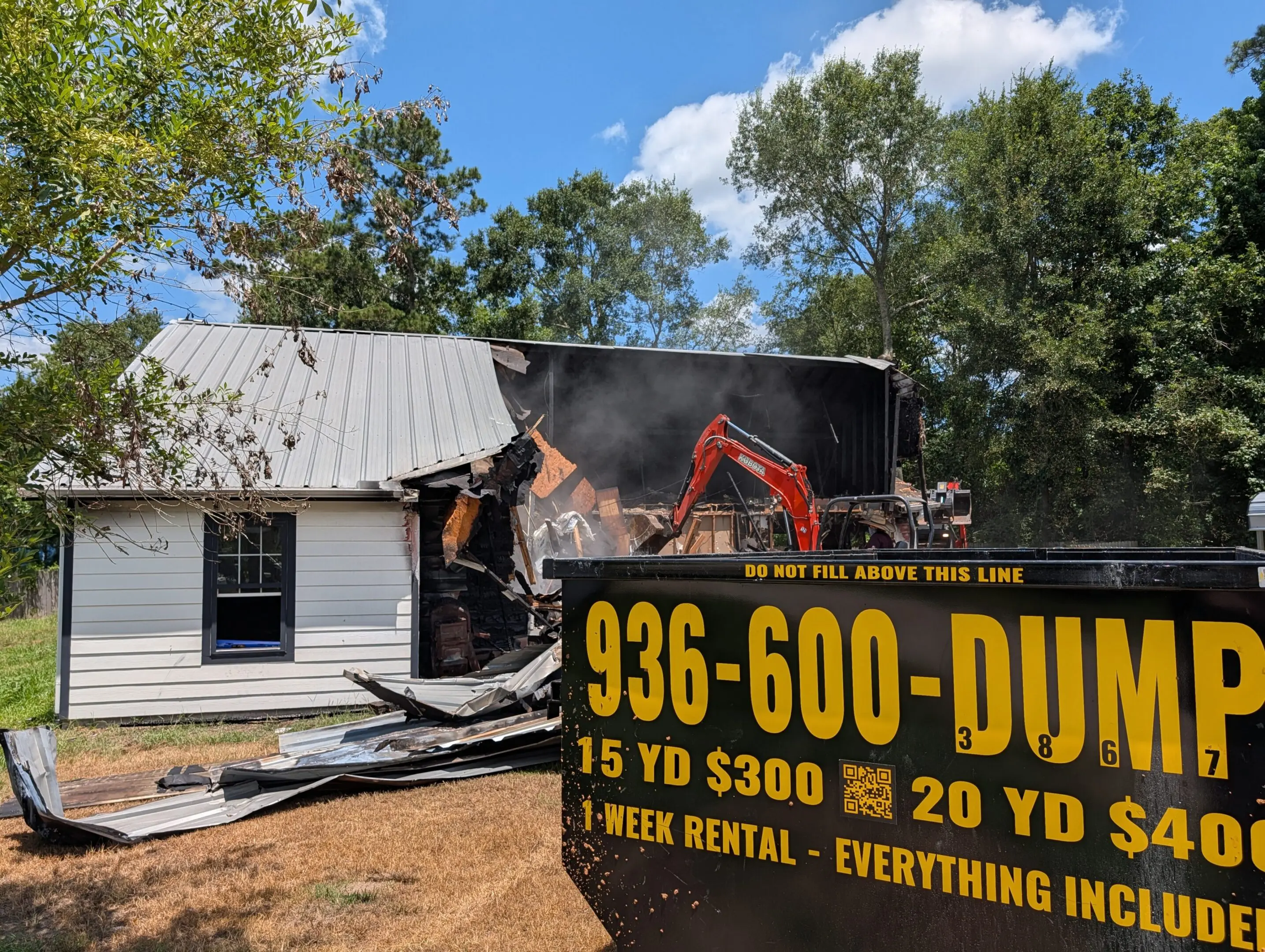 936-600-DUMP excavator tearing down a residential house in Montgomery County TX with branded roll-off dumpster on site