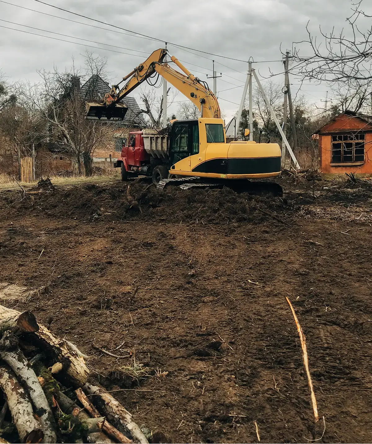 Yellow excavator loading dump truck on vacant lot