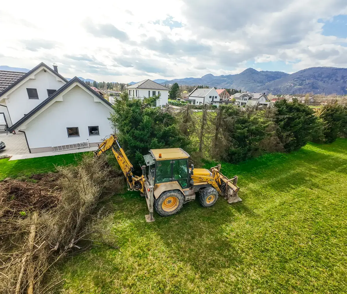 Yellow backhoe clearing brush near suburban homes